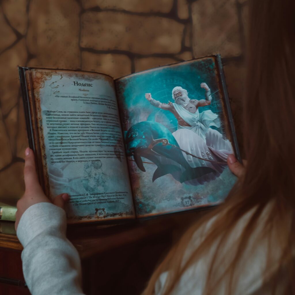 A child with long hair holds an open book. The child has long hair, suggesting they are female. The book has an image from Greek mythology.